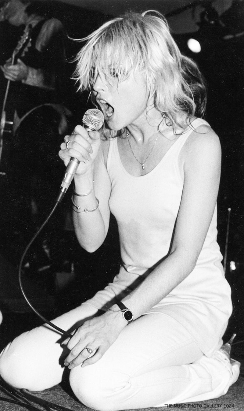 Debbie Harry singing on her knees during a performance, photographed by Ebet Roberts.