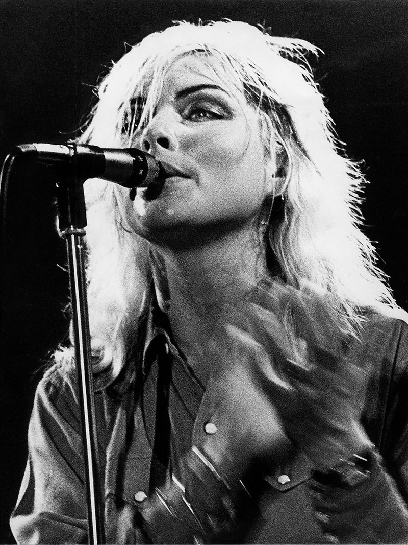 Blondie performing at the microphone under stage light in 1978. Photograph by Gijsbert Hanekroot.