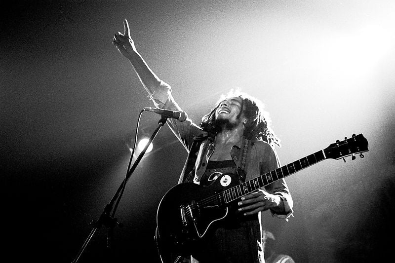 Bob Marley performing with guitar and one arm raised in 1977. Photograph by Gijsbert Hanekroot.
