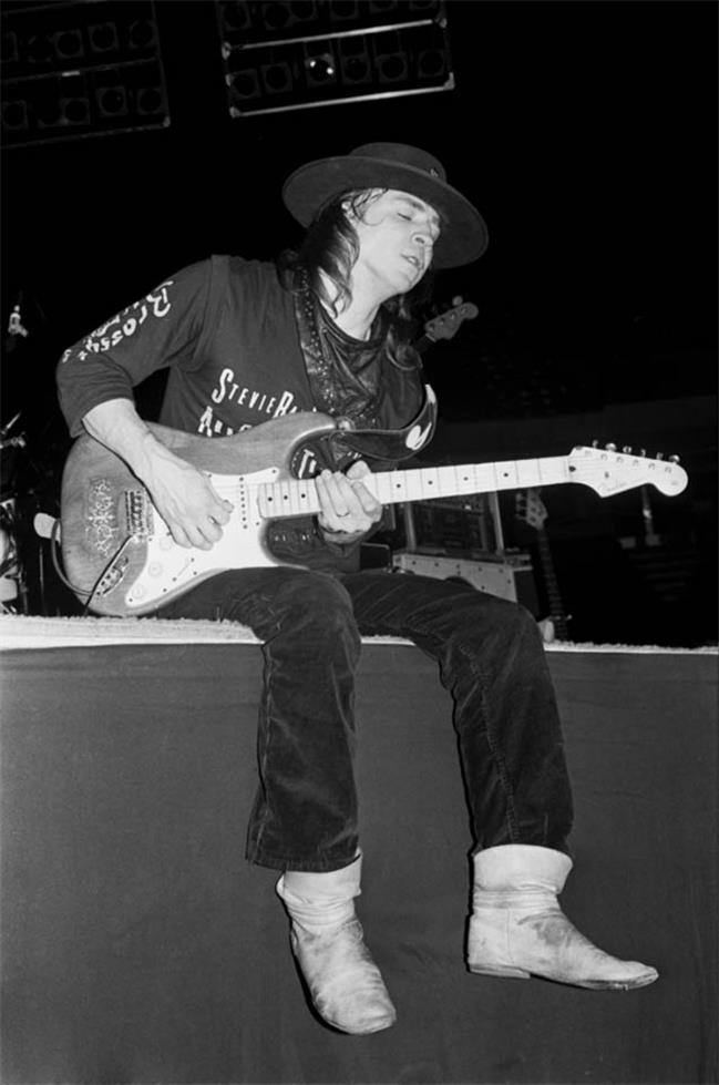 Stevie Ray Vaughan seated with his guitar and white boots, photographed by Charlyn Zlotnik, 1989.