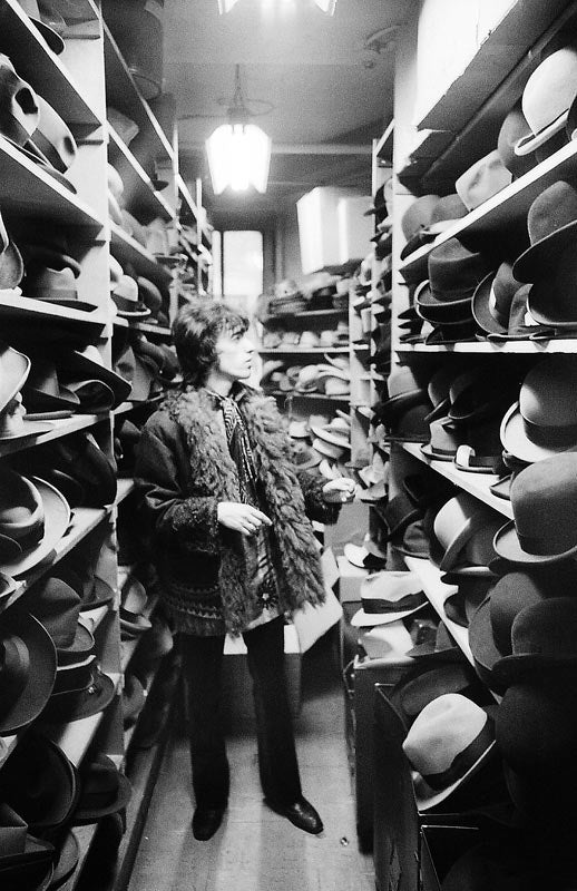 Bill Wyman of the Rolling Stones trying on hats in a New York store, photographed by Michael Cooper, 1967.
