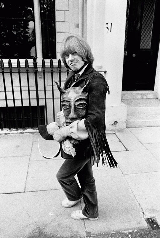Brian Jones of the Rolling Stones walking with a mask, London, photographed by Michael Cooper, 1968.