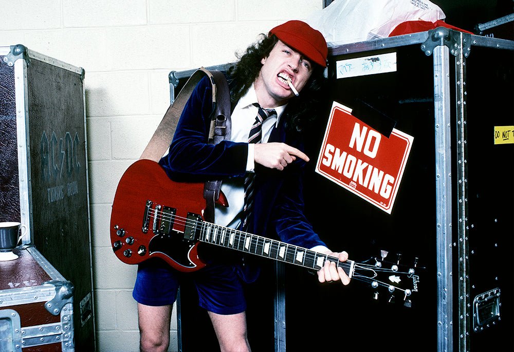 Angus Young of AC/DC backstage beside a No Smoking sign during the Flick of the Switch Tour, Florida, 1983, photographed by Mark Weiss.