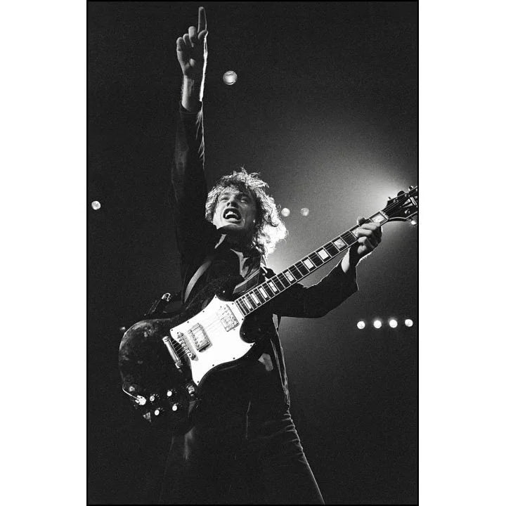 Angus Young of AC/DC performing live with his guitar, arm raised, at the Hammersmith Odeon, London, in 1979, photographed by David Corio.