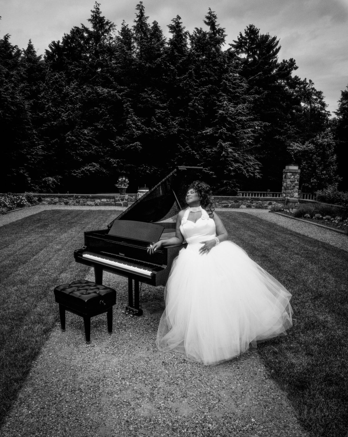 Aretha Franklin tilts her head back beside a grand piano in a garden setting. Photograph by Timothy White, Detroit, Michigan, 1993.