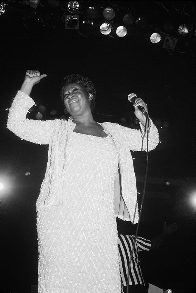 Aretha Franklin with one arm raised at the microphone in New York, photographed by Charlyn Zlotnik, 1982.