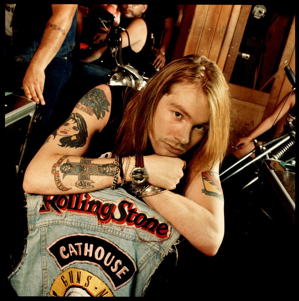 Axl Rose resting his tattooed arms on a denim vest, photographed by Timothy White in Asbury Park, New Jersey, 1988.