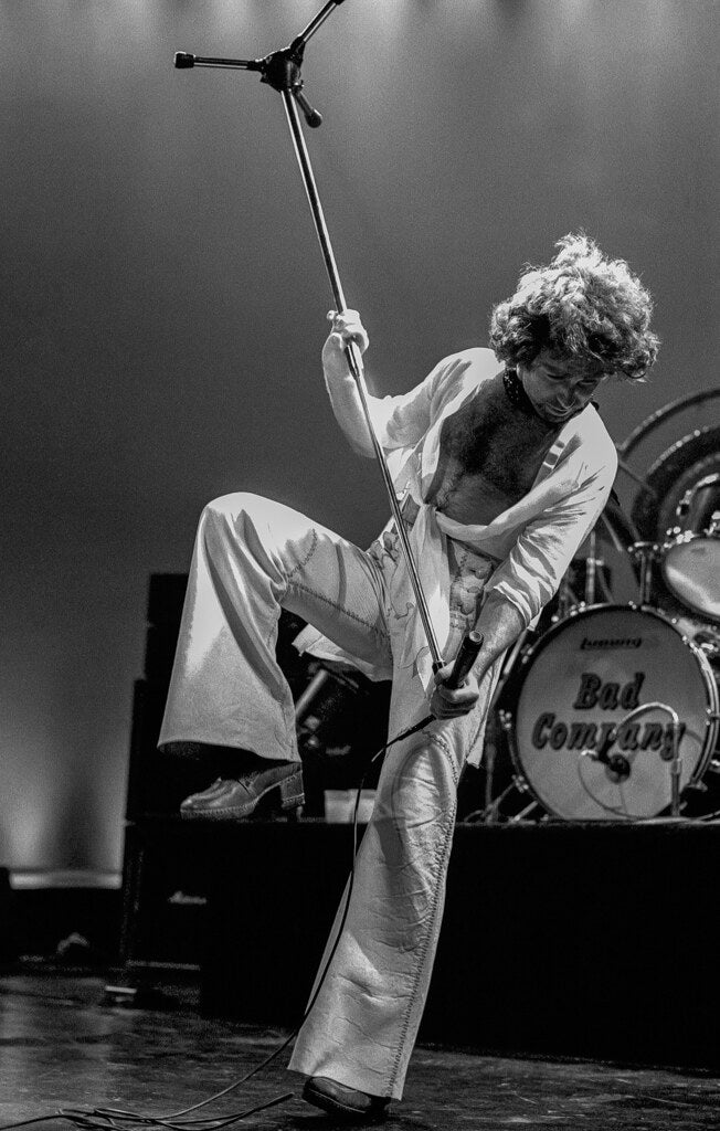 Bad Company's singer lifting the microphone stand overhead, in black and white, 1977, photographed by Lynn Goldsmith.