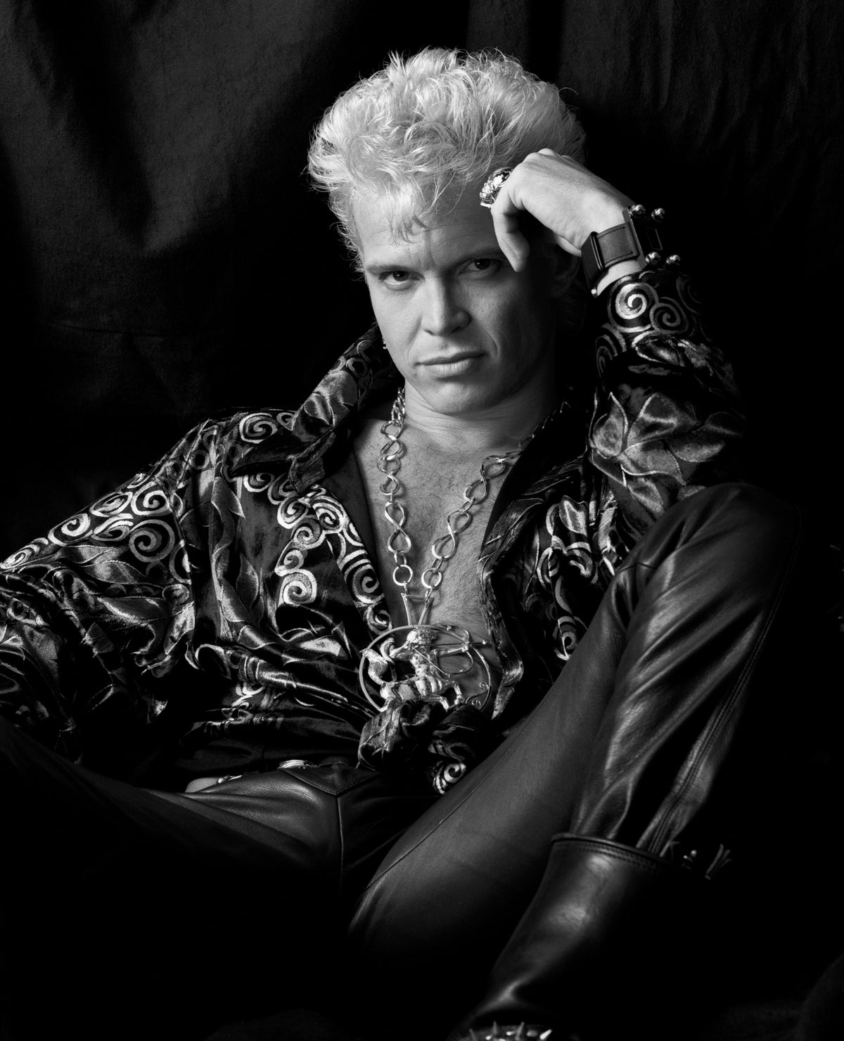 Billy Idol sits with one hand raised to his head, his patterned shirt picked out by directional light. Photograph by Timothy White, Beverly Hills, California, 1990.