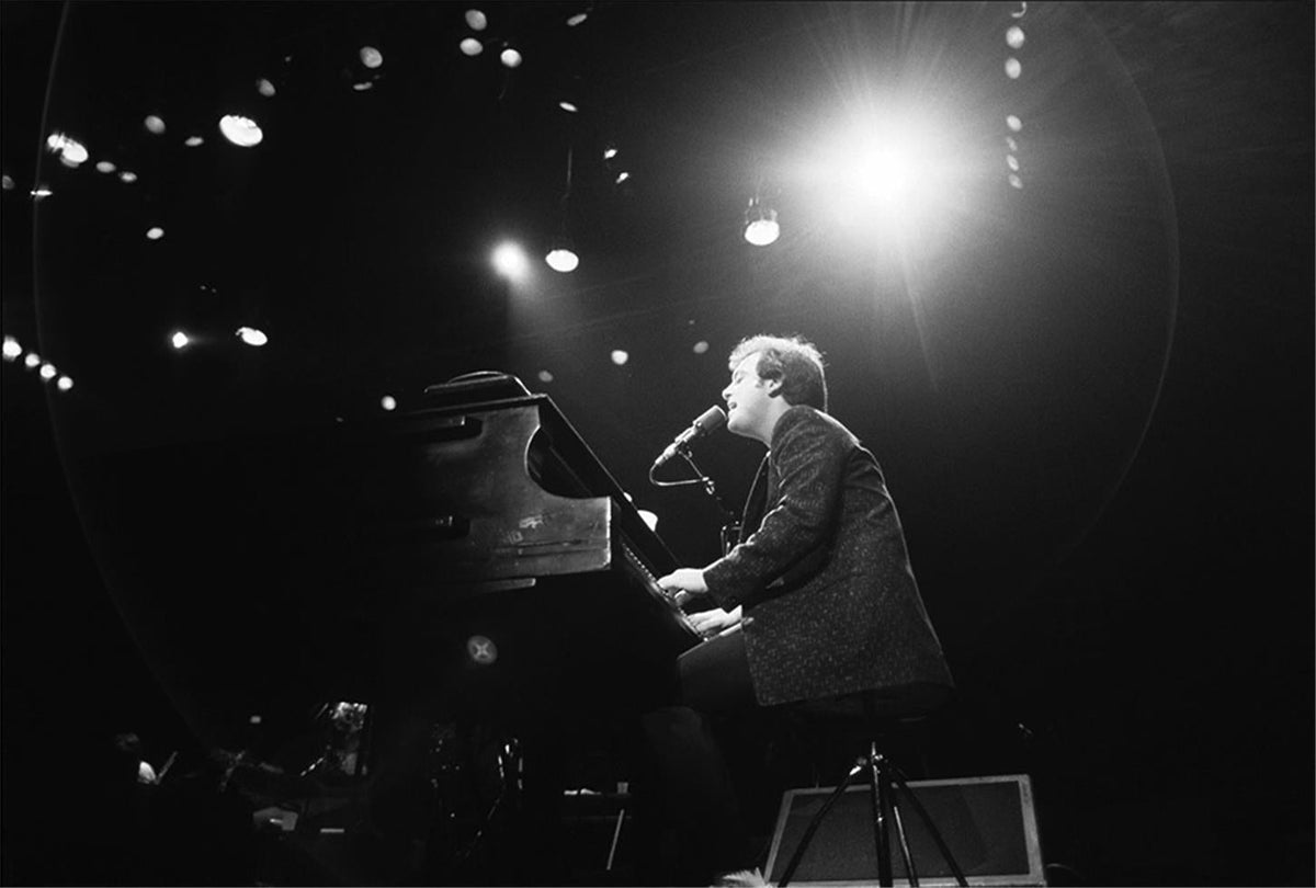 Billy Joel backlit at the grand piano on stage, photographed by Charlyn Zlotnik.