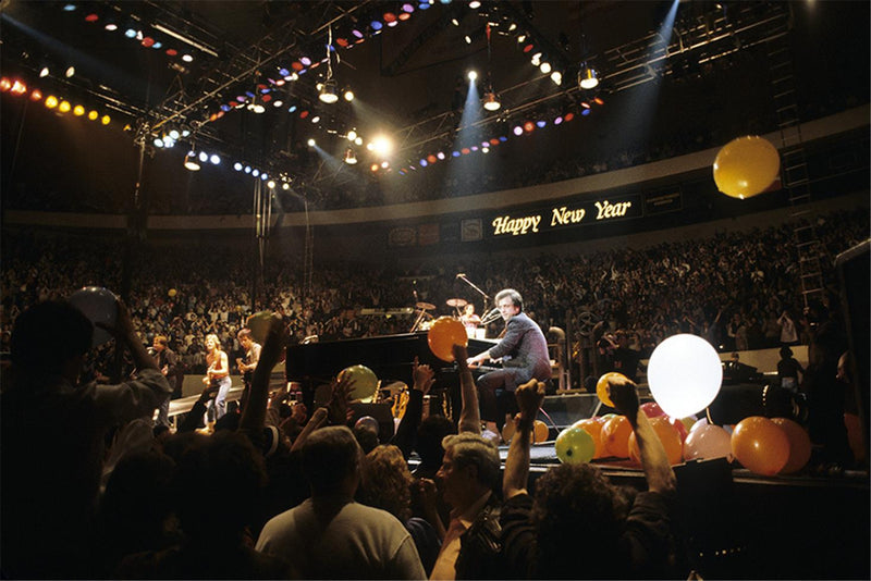 Billy Joel at the piano during a New Year's Eve arena show with balloons falling over the crowd, photographed by Charlyn Zlotnik.