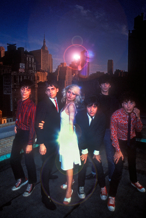 Blondie, six members in suits and sneakers with Debbie Harry in a white dress, on a New York City rooftop at dusk with the Manhattan skyline behind, photographed by Martyn Goddard, 1978.