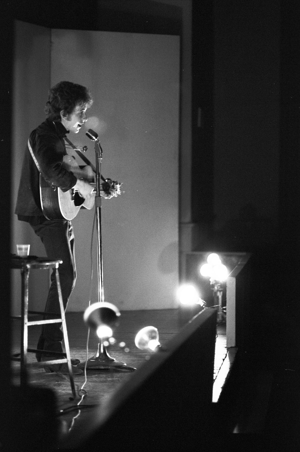 Bob Dylan on Stage with Footlights, Unknown Location, 1964; photograph by John Byrne Cooke.