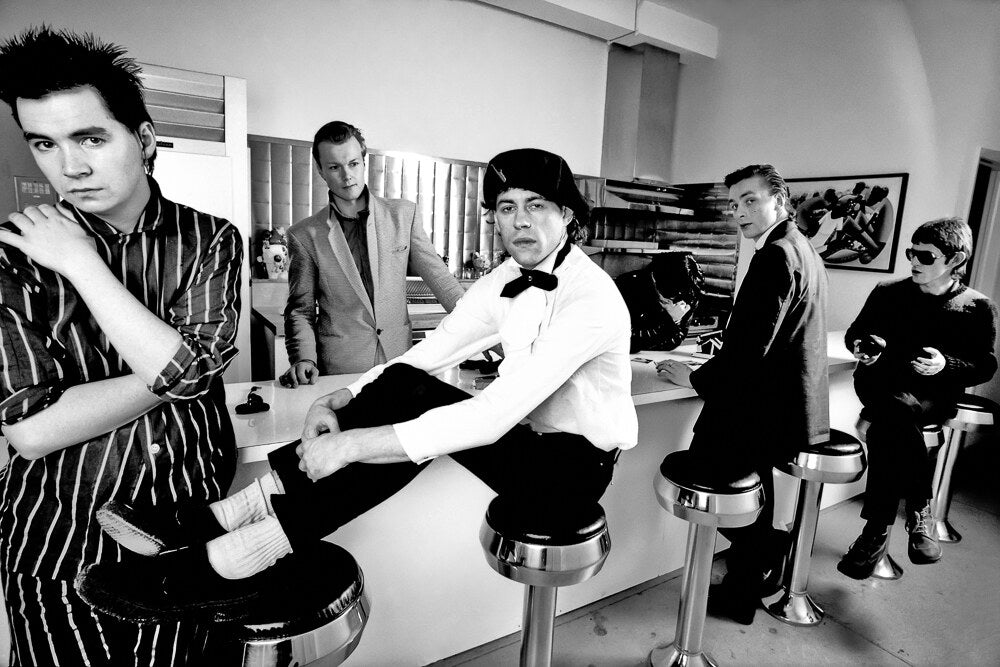 The Boomtown Rats lounging on diner stools, in black and white, 1981, photographed by Lynn Goldsmith.