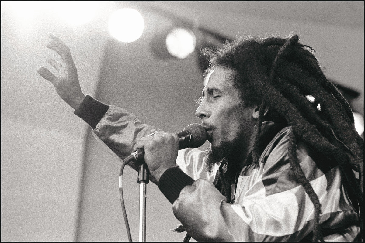 Bob Marley singing into a microphone with his eyes closed and one hand raised, Crystal Palace Bowl, London, 1980, photographed by David Corio.