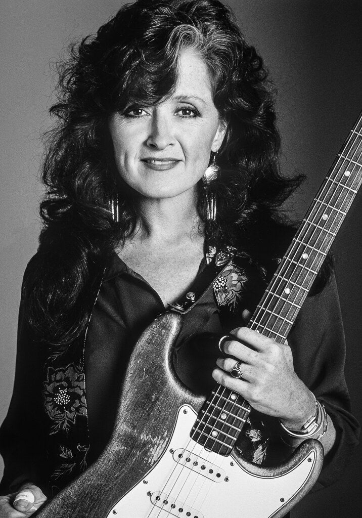 Bonnie Raitt holding her electric guitar, in black and white, 1989, photographed by Lynn Goldsmith.