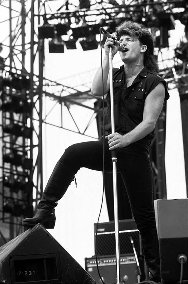 Bono of U2 standing on a stage monitor in daylight, photographed by Charlyn Zlotnik, 1983.
