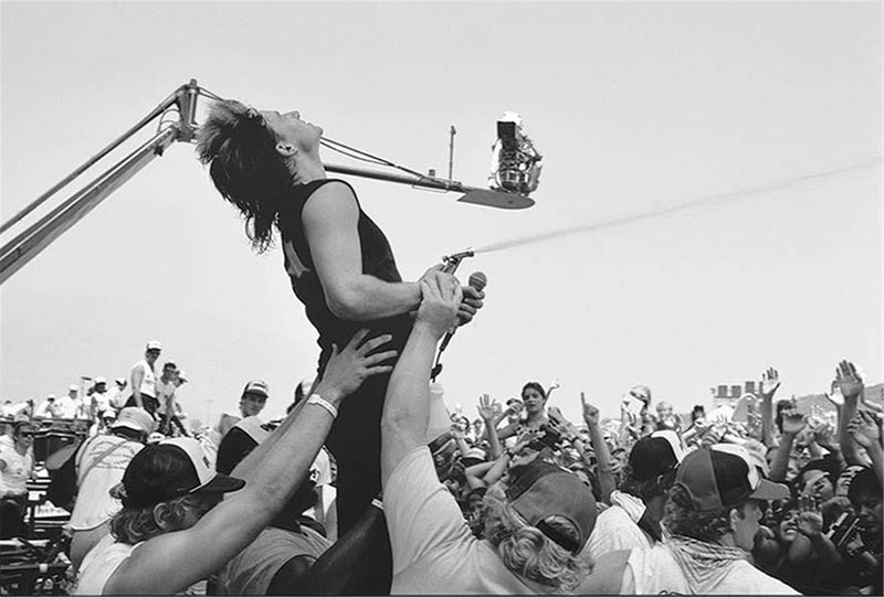 Bono of U2 carrying the white flag on a lighting rig above the crowd, photographed by Charlyn Zlotnik, 1983.