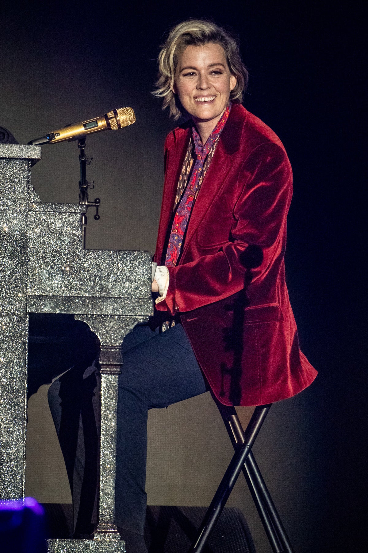 Brandi Carlile seated beside a piano in a red velvet suit, in color, 2024, photographed by Lynn Goldsmith.