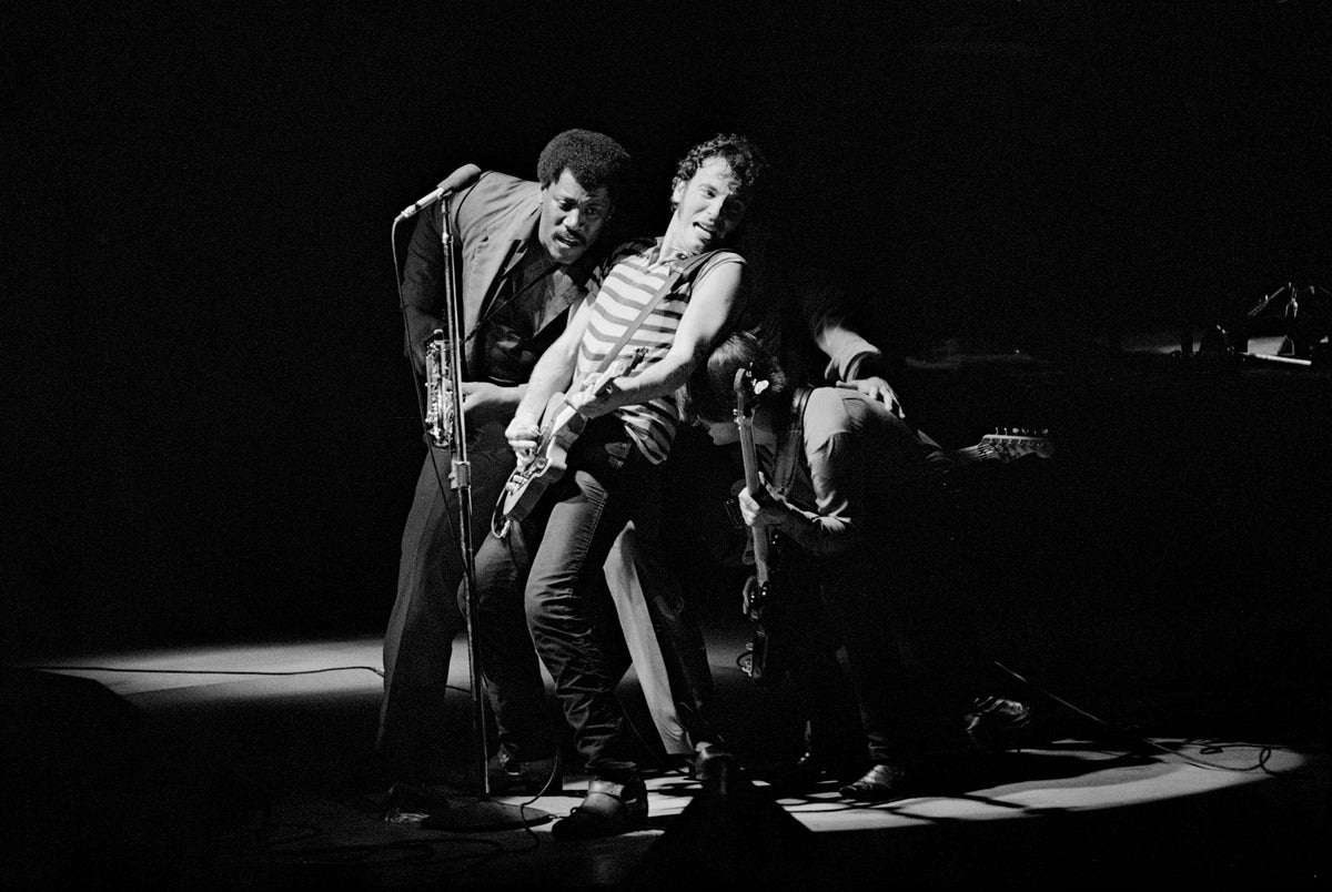 Bruce Springsteen playing guitar in a spotlight with members of the E Street Band on stage at Wembley Arena, London, 1981, photographed by David Corio.