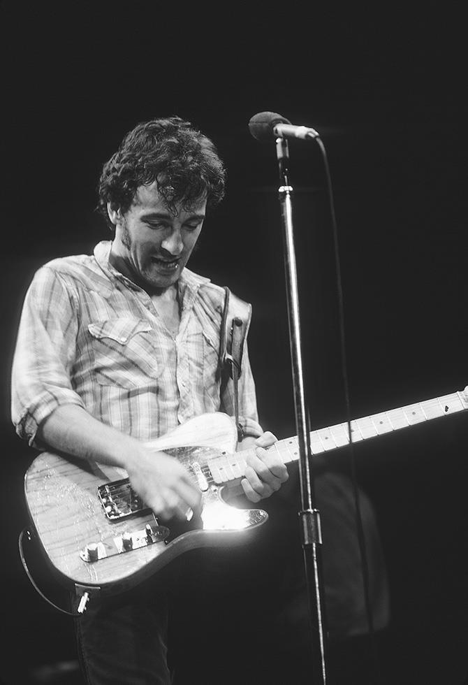 Bruce Springsteen at the microphone in a checked shirt playing his Telecaster, photographed by Charlyn Zlotnik.