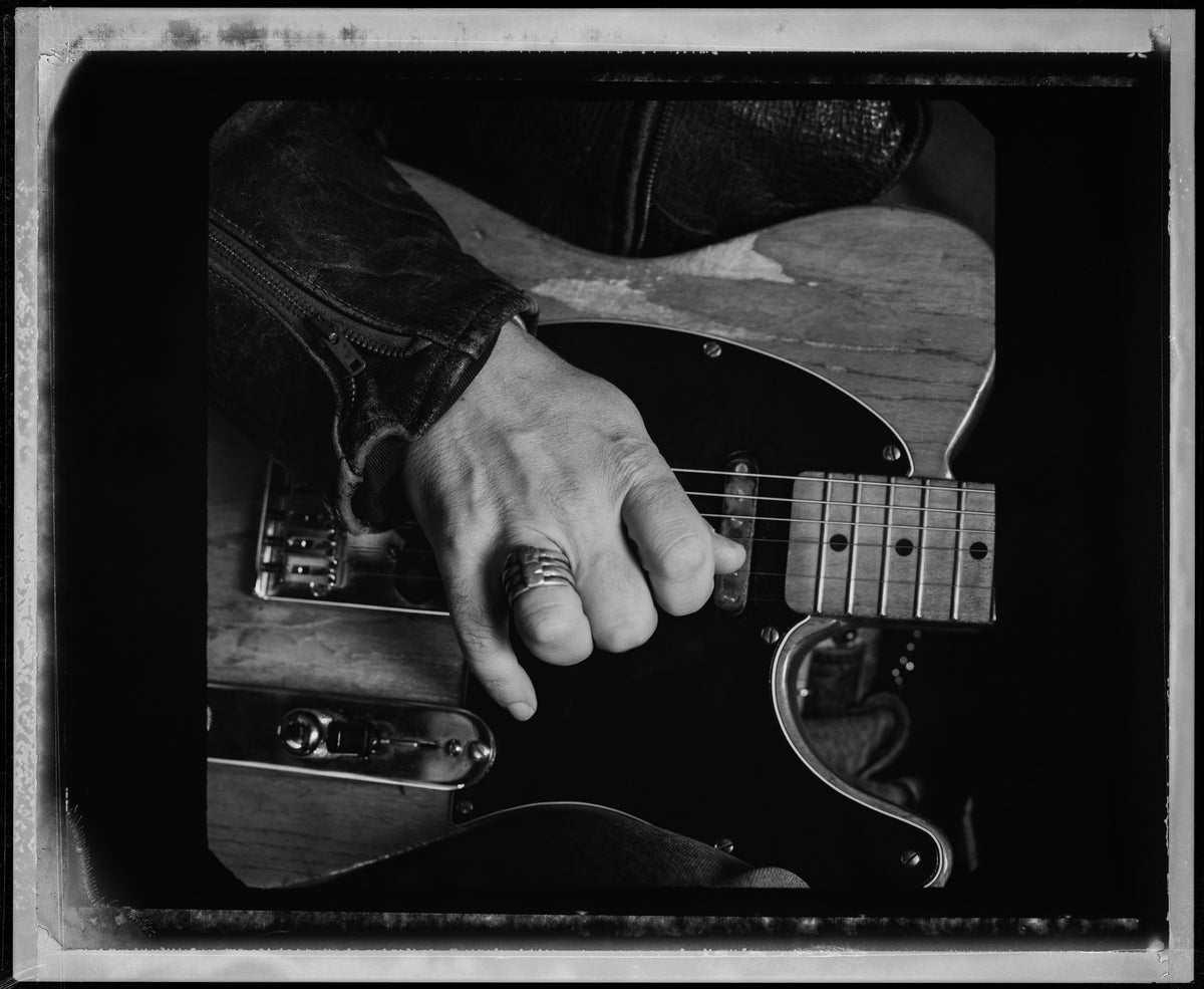 A close view isolates Bruce Springsteen’s hand resting across the strings and body of an electric guitar. Photograph by Timothy White, Malibu, California, 1991.
