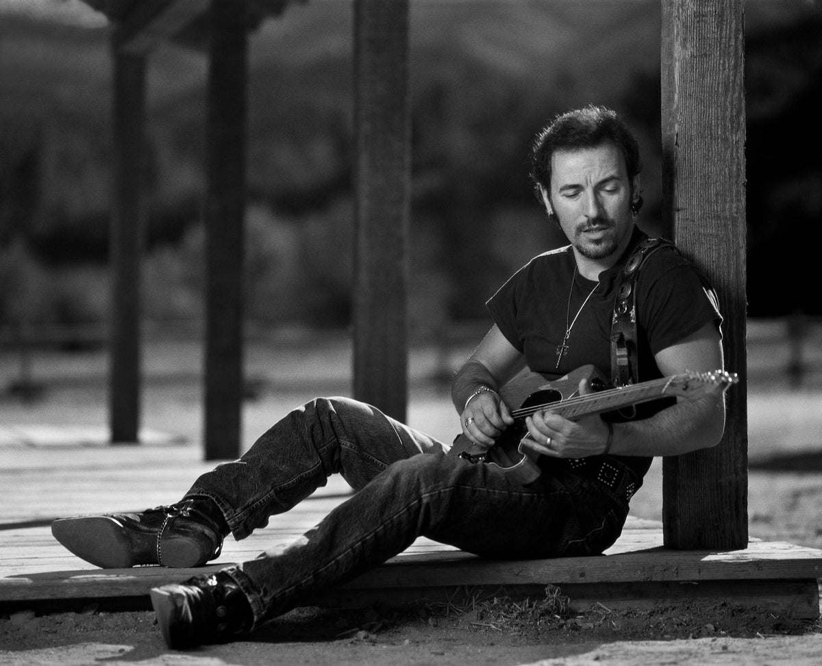 Bruce Springsteen sits on the ground with an acoustic guitar across his lap. Photograph by Timothy White, Malibu, California, 1991.