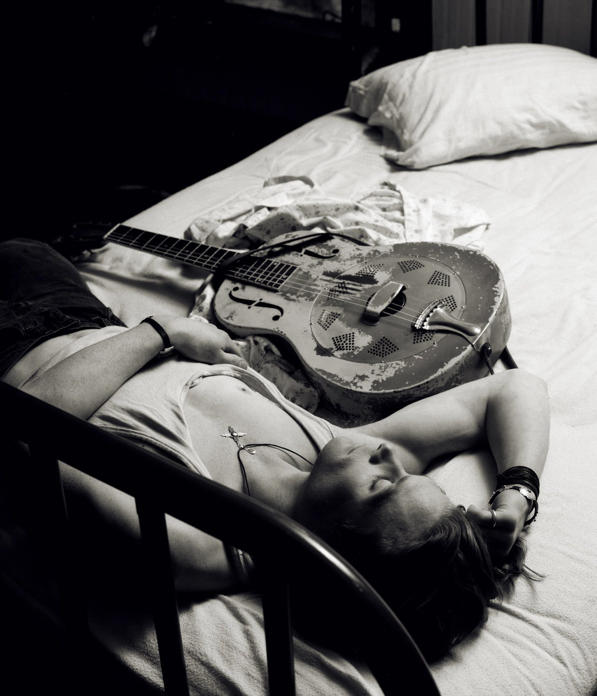 Chris Whitley lies on a bed with a guitar resting across his body in an intimate overhead view. Photograph by Timothy White, New Orleans, Louisiana, 1991.