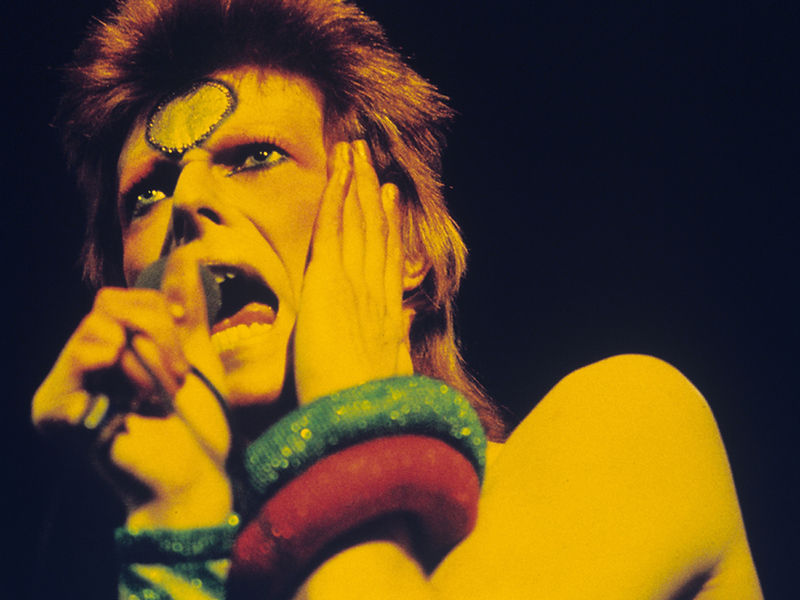 David Bowie performing in saturated yellow and red stage light in 1973. Photograph by Gijsbert Hanekroot.