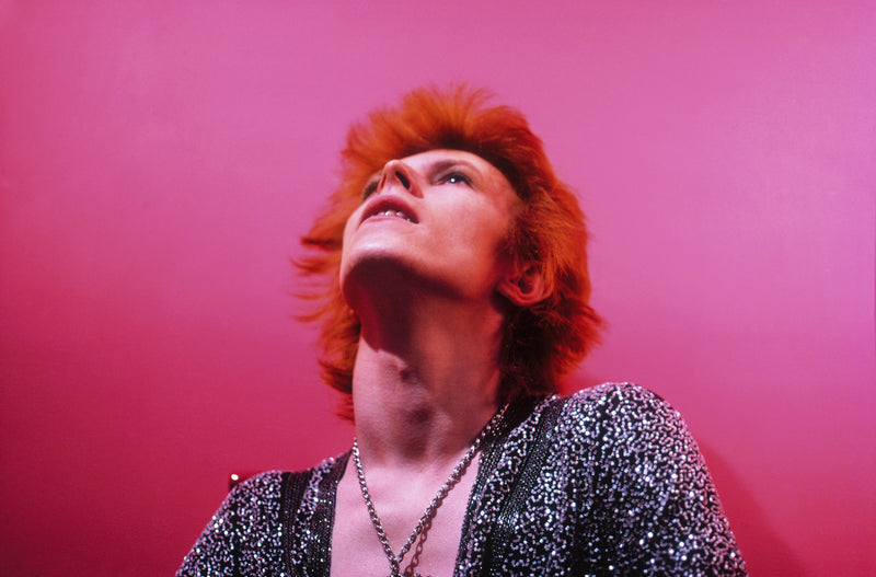David Bowie looking upward against a pink background at Haddon Hall, 1972, photographed by Mick Rock