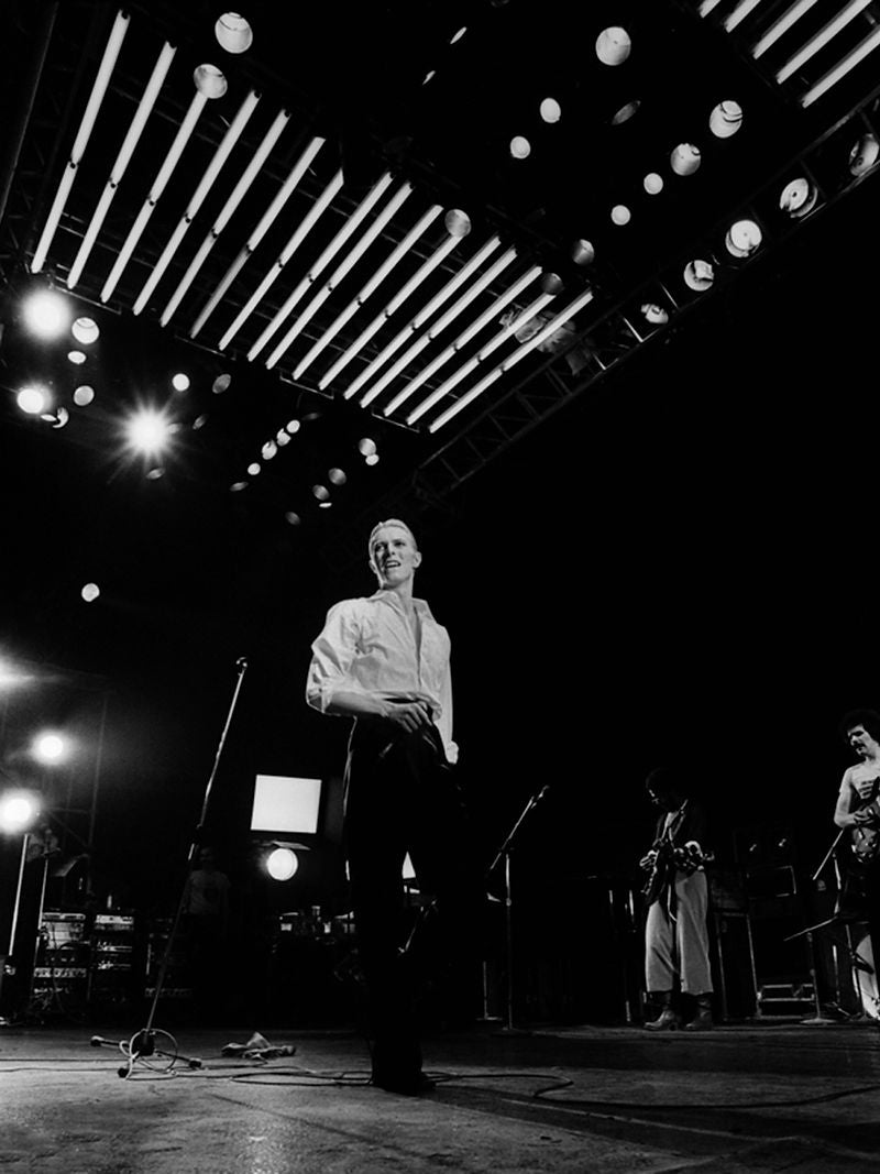 David Bowie standing beneath a grid of stage lights in 1976. Photograph by Gijsbert Hanekroot.