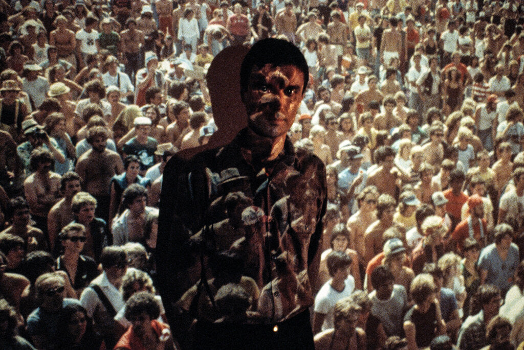 David Byrne double-exposed over a dense concert crowd, in color, 1980, photographed by Lynn Goldsmith.