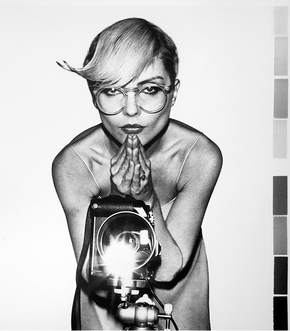 Debbie Harry in clear-framed glasses leaning over a camera on a tripod, Gramercy Park Hotel, New York City, black-and-white photograph by Martyn Goddard, 1978.