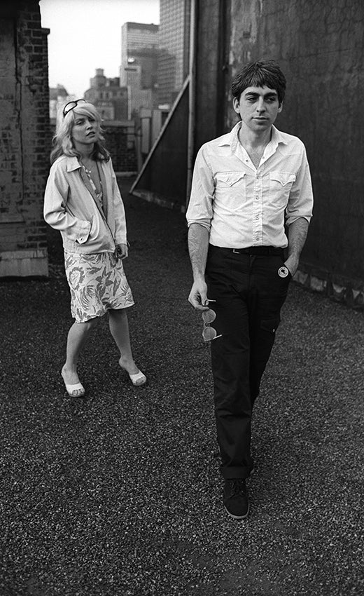 Chris Stein walking toward the camera with Debbie Harry behind him on the Record Plant studios rooftop, New York City, black-and-white photograph by Martyn Goddard, 1978.