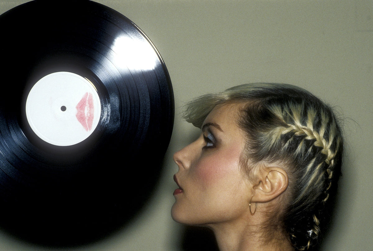 Debbie Harry in profile with braided hair facing a vinyl record with a lipstick kiss on its label, Parallel Lines picture disc cover, photographed by Martyn Goddard, 1978.