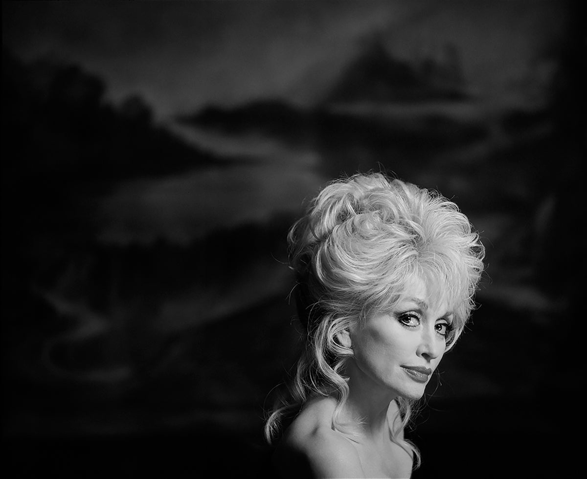 Dolly Parton turns toward the camera against a softly textured dark backdrop. Photograph by Timothy White, New York City, 1994.