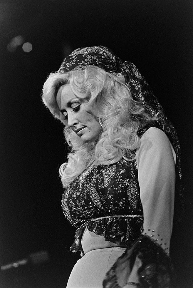Dolly Parton singing on stage in a beaded outfit and headscarf, photographed by Charlyn Zlotnik.