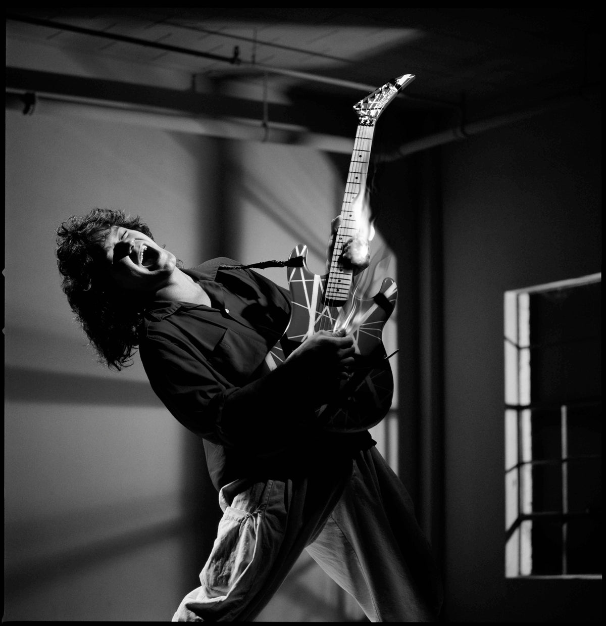 Eddie Van Halen leans backward while lifting his electric guitar in a forceful, diagonal pose. Photograph by Timothy White, Hollywood, California, 1988.