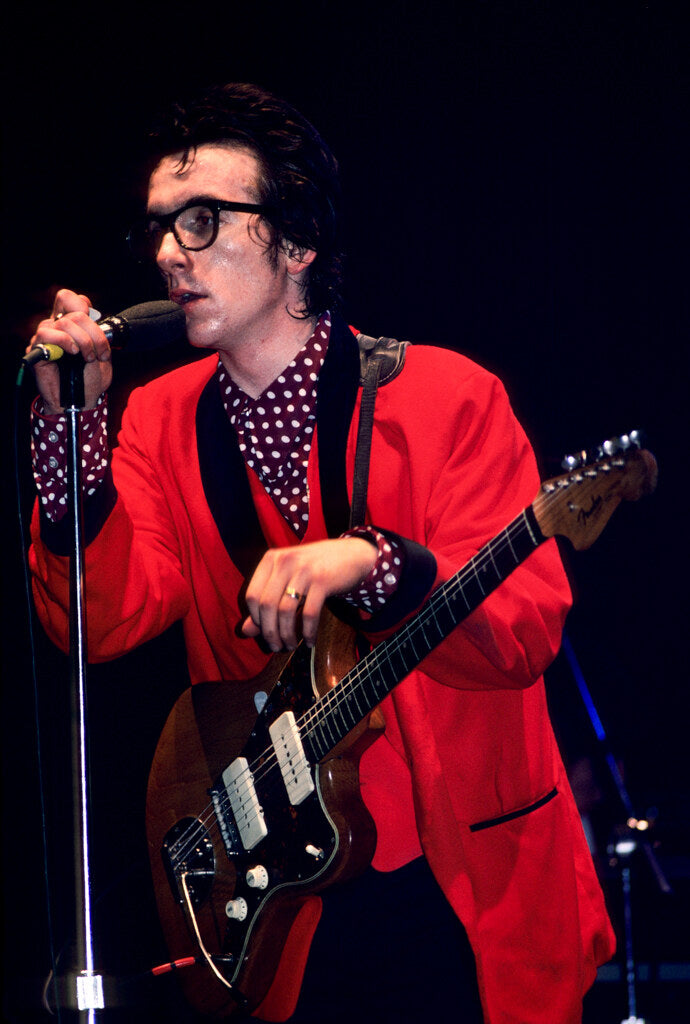 Elvis Costello on stage in a red jacket and polka-dot shirt, in color, 1977, photographed by Lynn Goldsmith.