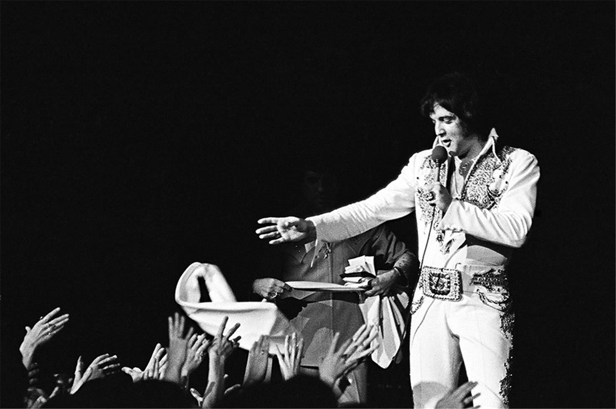 Elvis Presley leaning down toward the audience with hands reaching up from the crowd, photographed by Charlyn Zlotnik, 1977.
