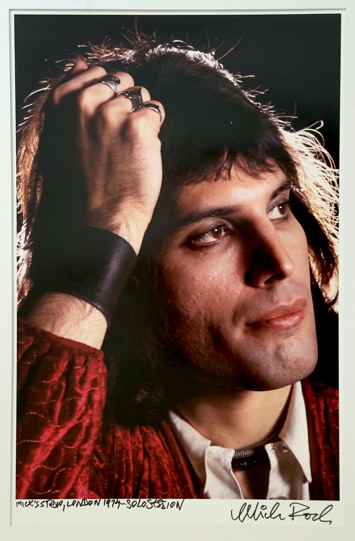 Freddie Mercury during a 1974 solo session at Mick Rock's London studio, hand in his hair, in a crimson jacket — colour photograph by Mick Rock, a signed, hand-titled late print.