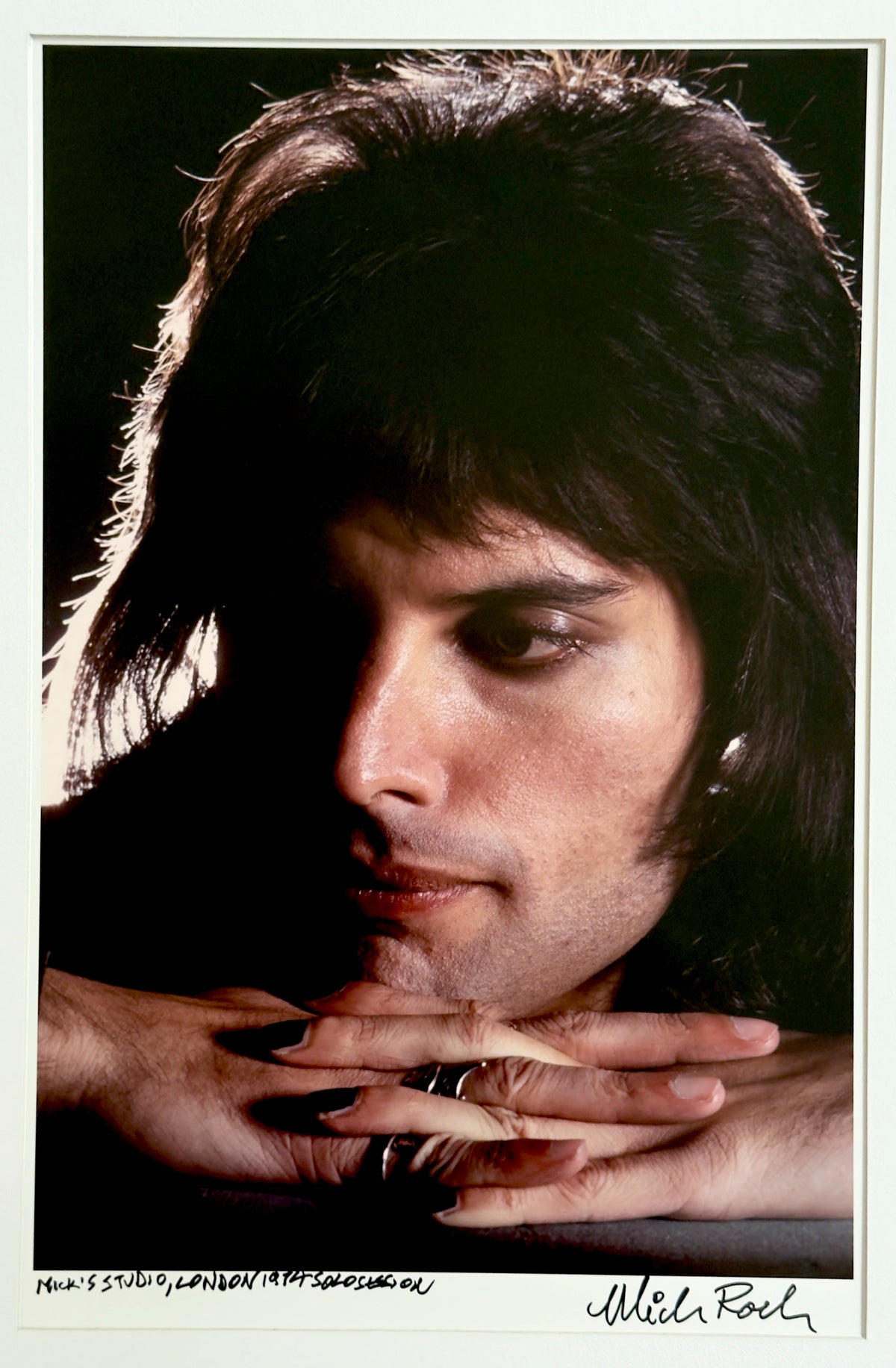 Freddie Mercury during a solo session at Mick Rock's London studio, 1974, chin resting on laced hands — colour photograph by Mick Rock, a signed, hand-titled late print.