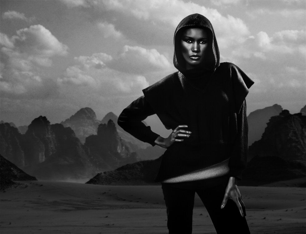 Grace Jones in a hooded top before a mountain landscape, in black and white, 1979, photographed by Lynn Goldsmith.