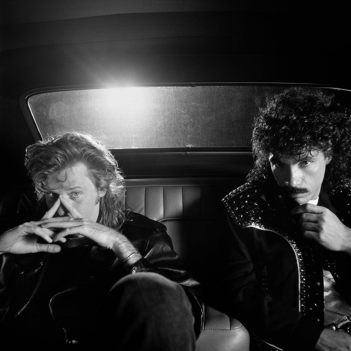 Hall & Oates sit inside a car, their faces framed by the windshield and the dark interior. Photograph by Timothy White, Burlington, Vermont, 1988.