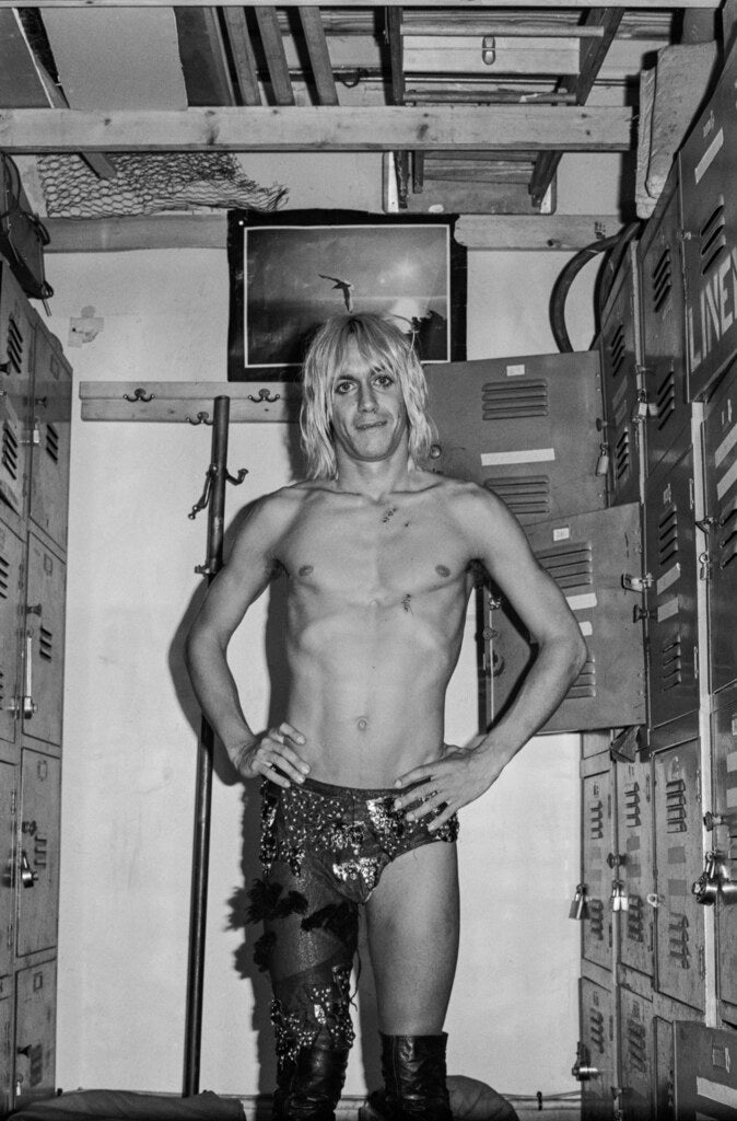 Iggy Pop shirtless in a locker-lined dressing room, hands on hips, 1973, photographed by Lynn Goldsmith.