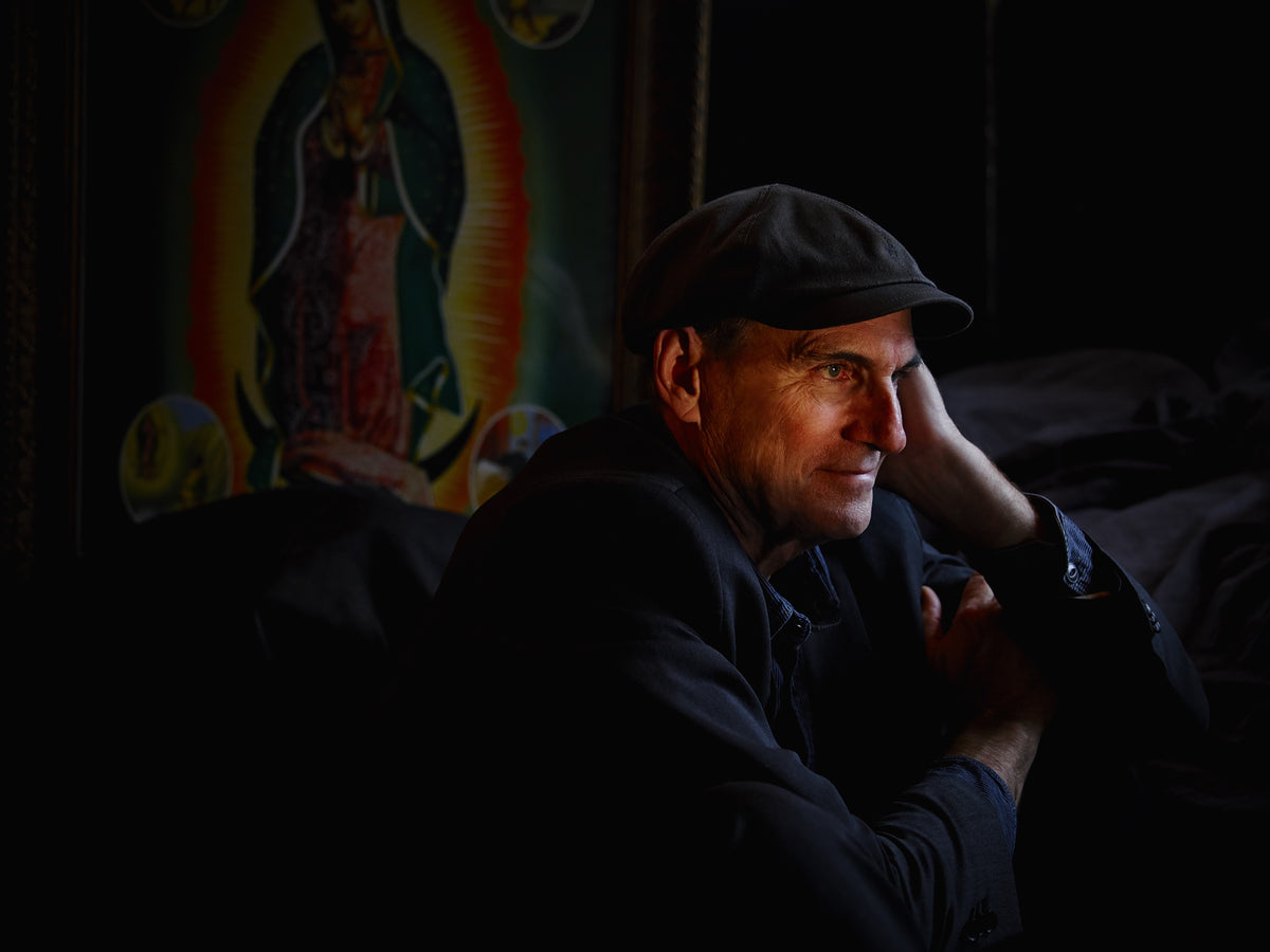 James Taylor rests his head against one hand in a warmly colored interior, with an image of Our Lady of Guadalupe behind him. Photograph by Timothy White, Stockbridge, Massachusetts, 2014.