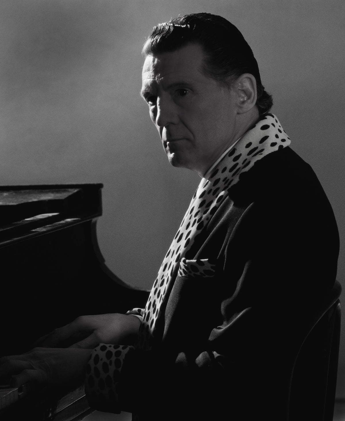 Jerry Lee Lewis sits at a piano in profile, his face and patterned scarf emerging from a dark background. Photograph by Timothy White, Memphis, Tennessee, 1989.