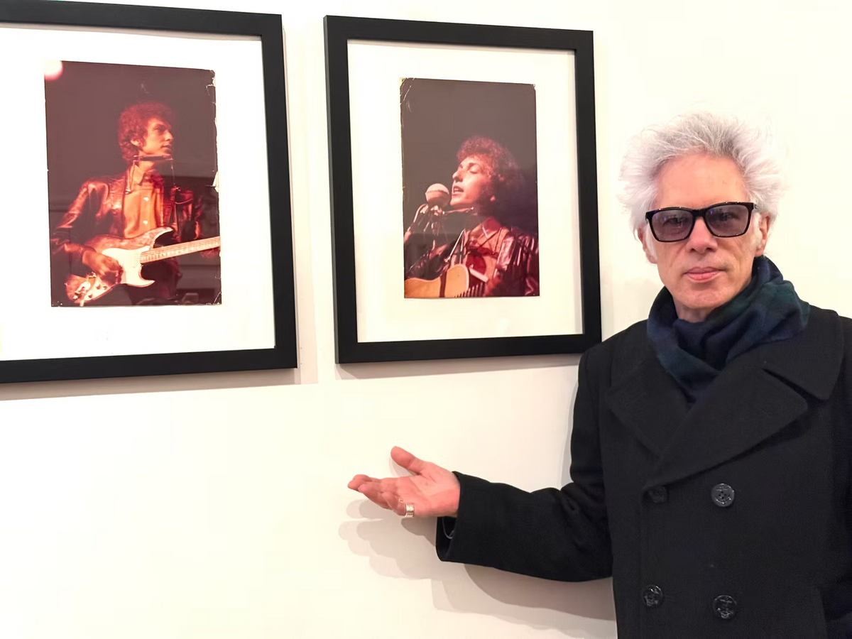 Filmmaker Jim Jarmusch standing beside two vintage gelatin silver prints of Bob Dylan photographed by Bob Gruen during the 1965 Newport Folk Festival, exhibited at The Music Photo Gallery, SoHo, New York.