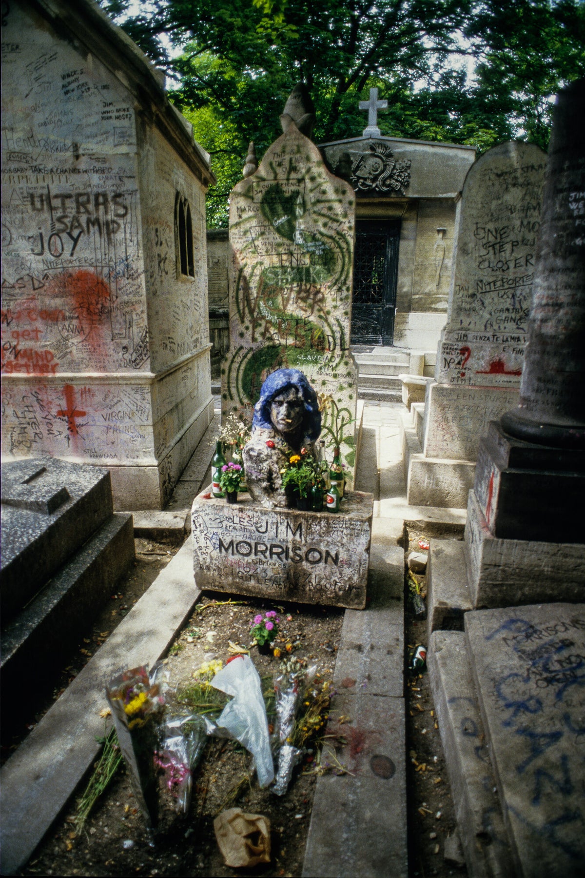 Jim Morrison's grave at Père Lachaise covered in graffiti and flowers, in color, 1986, photographed by Lynn Goldsmith.