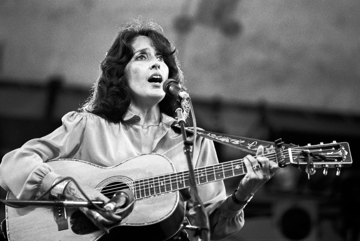 Joan Baez singing with an acoustic guitar outdoors, in black and white, 1979, photographed by Lynn Goldsmith.